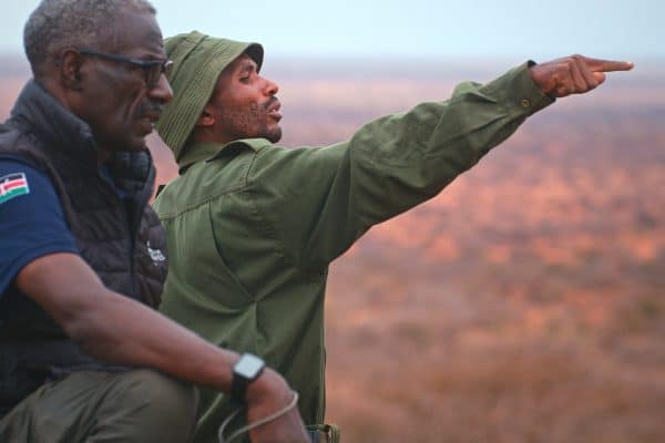 two kenyan men one in a green hat pointing