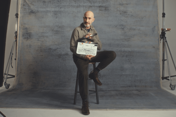 Bald man sat on a stool in a studio with a clapperboard