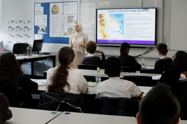 A woman in a head scarf teaches a diverse class of pupils in the UK