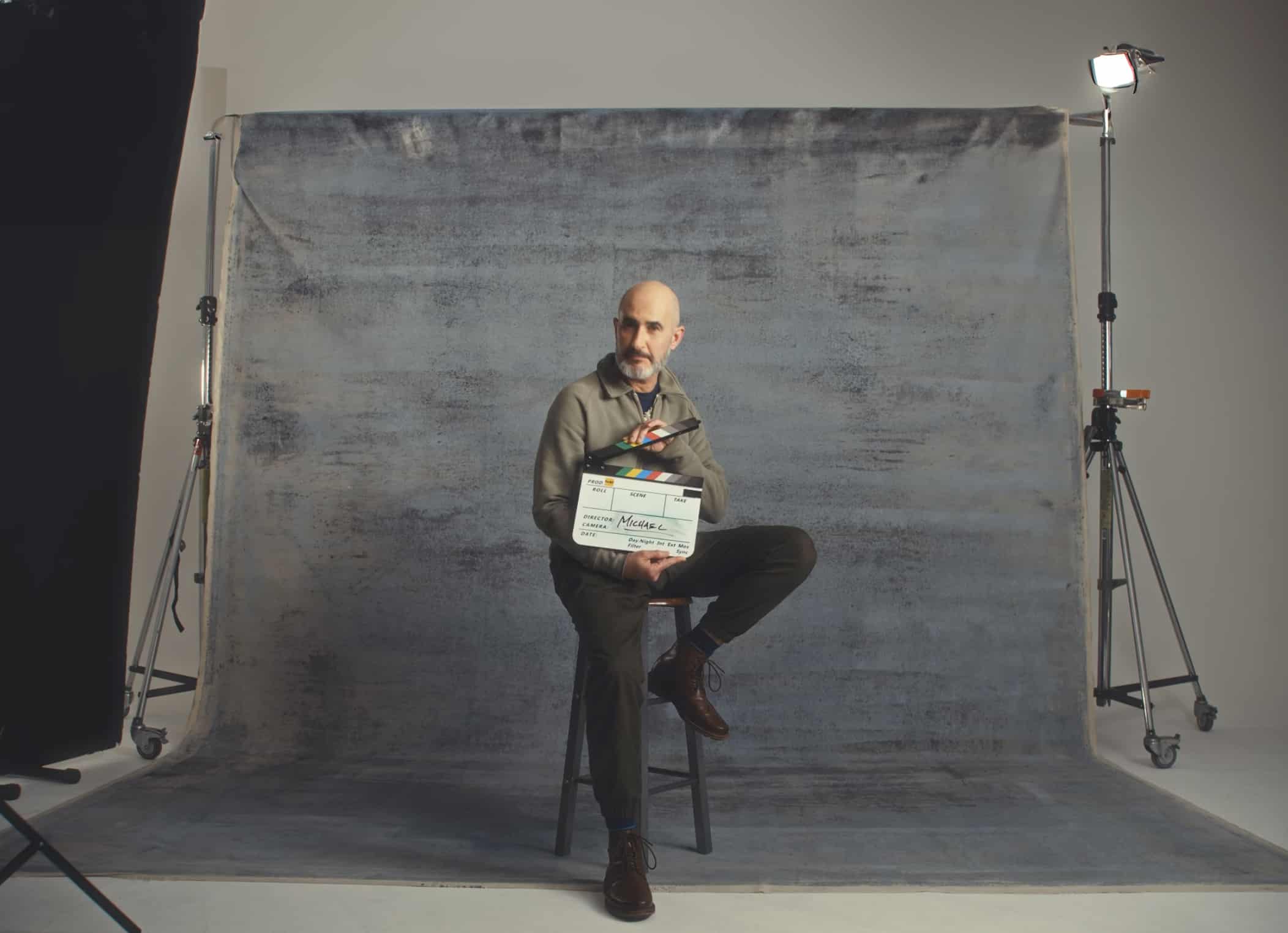 A man sat on a stoll in an interview holding a clapperboard