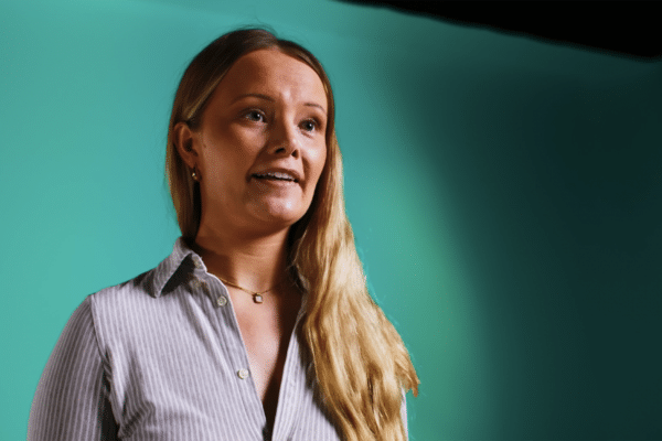 Interview shot of a professional lady with blonde hair against a green background. Low three quarter angle shot.